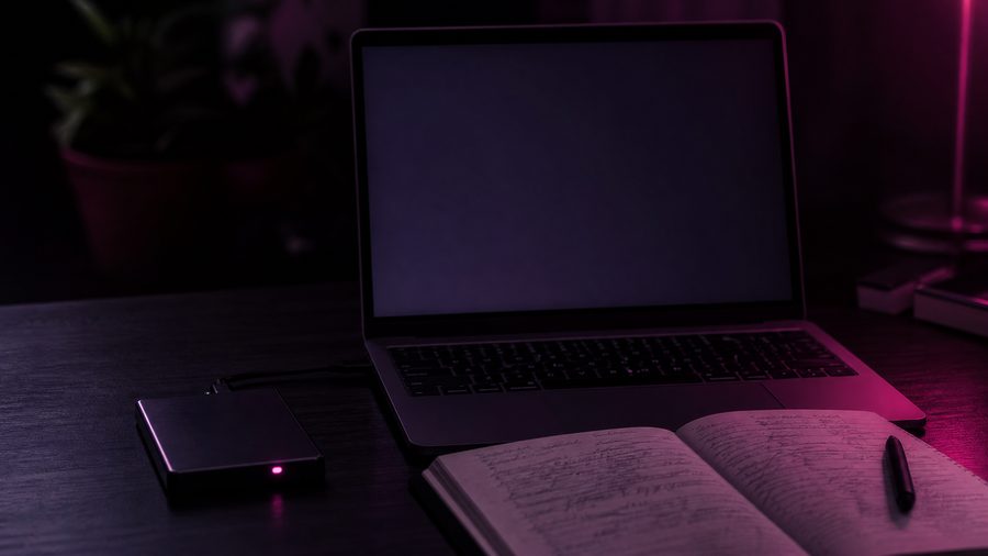 An open laptop with a blank dim screen beside a small external drive with a pink status light